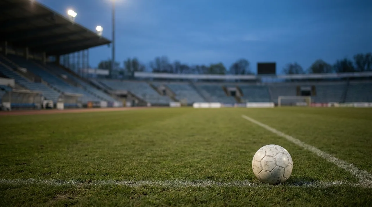 Un ballon de football sur la pelouse d’un stade vide au crépuscule.